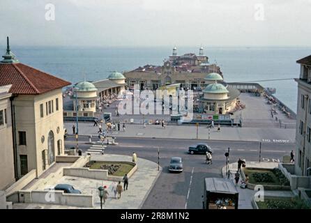 Ein 1963-Grad-Blick auf den Hastings Pier und seine Art déco-Gebäude am Meer in Hastings, East Sussex, England, Großbritannien. Schilder zeigen die verschiedenen Attraktionen: Restaurant, Unterhaltung, Café, Ballsaal und Rock Shop. Die Liegestühle sind prominent und eine Live-Musikbühne ist im Zentrum. Erbaut im Jahr 1872 und genießt seine Blüte in den 1930er Jahren, als die Gebäude ein Art déco-Facelift erhielten und das Theater neu aufgebaut wurde. Das Gebäude erlitt 1990 schwere Sturmschäden und wurde 2008 geschlossen, Ein schwerer Brand Beschädigte den Pier 2010. 2016 eröffnete sie wieder – ein klassisches Foto aus dem Jahr 1960er. Stockfoto