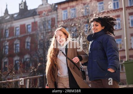 Weibliche Freunde gehen zusammen durch unsere Türen auf dem Fußweg in der Stadt Stockfoto