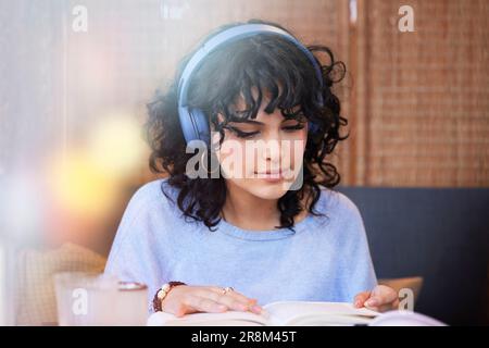 Junge Frau mit Kopfhörern, die beim Lesen eines Buches Musik oder Podcast hört Stockfoto