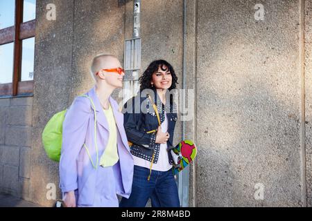 Lächelnde weibliche Freunde oder schwule Paare, die Skateboards tragen und zusammen gehen Stockfoto