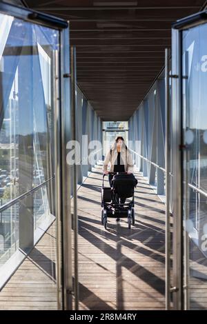 Blick auf eine Frau im Elternurlaub, die einen Kinderwagen durch einen erhöhten Gang schiebt Stockfoto