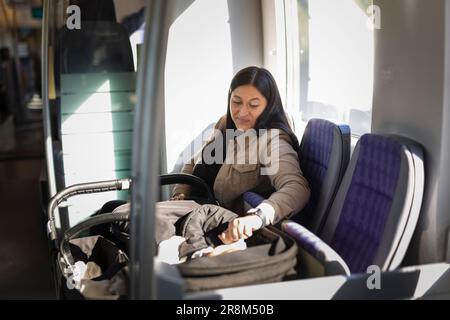 Lächelnde Frau im Zug, die das Baby im Kinderwagen überprüft Stockfoto