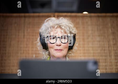 Seniorin mit Kopfhörern, die ein Tablet verwenden Stockfoto