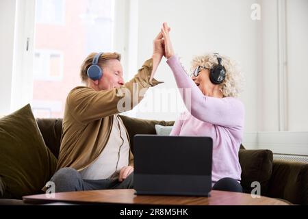 Ältere Männer und Frauen geben sich gegenseitig High Five, während sie im Wohnzimmer vor dem digitalen Tablet sitzen Stockfoto