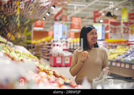 Lächelnde Frau, die im Supermarkt steht und Apfel hält Stockfoto