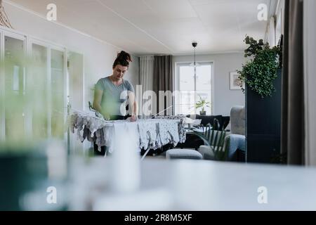 Schwangere Frau, die Hausarbeit macht und Babykleidung an einen Trockenständer hängt Stockfoto