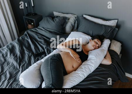 Schwangere Frau, die auf einem Schwangerschaftskissen auf dem Bett schläft Stockfoto