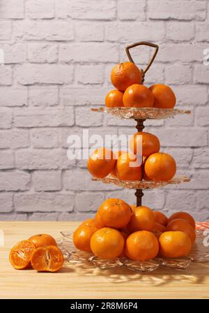 Antike Kristallschale Mit Kleinen Orangen. Dessert mit Backsteinwand im Hintergrund Stockfoto