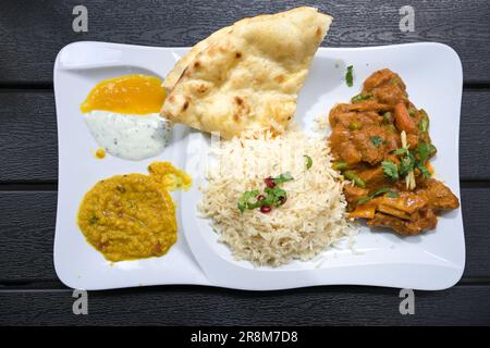 Indisches Rindfleischgericht mit Sauce, Reis, Brot, Linsen und Dips, serviert auf einem weißen Teller und einem dunklen Tisch, Blick von oben aus einem hohen Winkel, ausgewählter Foc Stockfoto