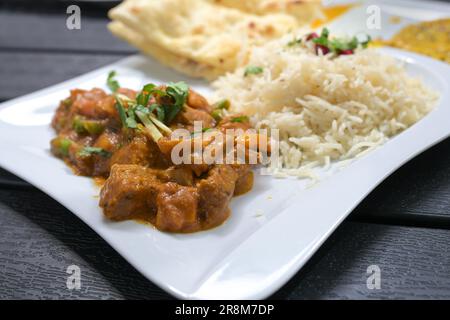 Indisches Gericht, Rindfleisch mit Gemüse in scharfer Sauce, Reis und Brot auf einem weißen Teller und einem schwarzen Tisch, ausgewählter Fokus, schmale Feldtiefe Stockfoto