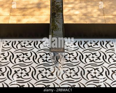 Nahaufnahme eines Gartenrills aus Metall, der in einen mit einem lasergeschnittenen Gitter bedeckten Pool in einem britischen Ausstellungsgarten fließt. Stockfoto