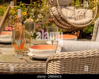 Gartentisch zum Abendessen im Freien mit Rattan-Hängestuhl in der Ferne. Stockfoto