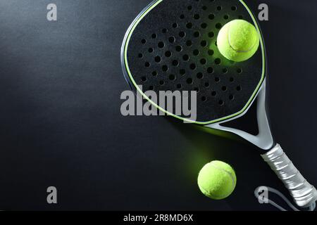 Hintergrund eines schwarz-weißen Paddle-Tennisschlägers und zwei Bälle auf einem schwarzen Tisch. Draufsicht. Stockfoto