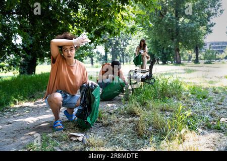 Junge Freiwillige räumen gemeinsam den Park auf, sammeln Müll und halten Müllsäcke. Verantwortungsbewusste Eltern und Freunde, die den öffentlichen Park von einem Stück säubern Stockfoto