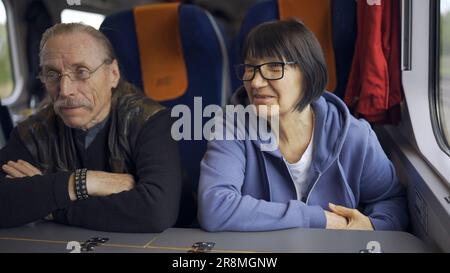 Ein älteres Paar fährt in einem Zugwaggon und redet miteinander Stockfoto