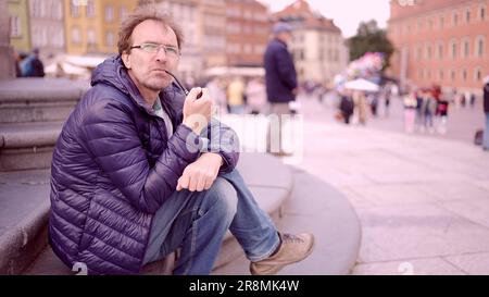 Warschau, Polen. 11. Juni 2023. Erwachsener Mann sitzt auf dem Platz und raucht eine Tabakpfeife auf dem Palastplatz, Warschauer Altstadt (Bild: © Andrey Nekrasov/ZUMA Press Wire) NUR REDAKTIONELLE VERWENDUNG! Nicht für den kommerziellen GEBRAUCH! Stockfoto