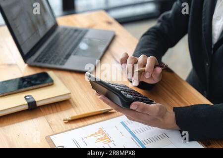 Nahaufnahme der Hände einer Geschäftsfrau mit einem Taschenrechner, um die Finanzen und Einnahmen des Unternehmens sowie das Budget zu prüfen. Geschäftsfrau, die die monatlichen Ausgaben berechnet Stockfoto
