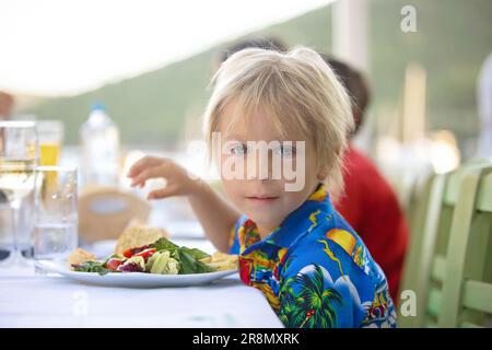 Süßes Kind, das im Sommer im Restaurant im Freien sitzt und Meeresfrüchte, Garnelen, Calamari, Tintenfisch und pommes frites isst Stockfoto