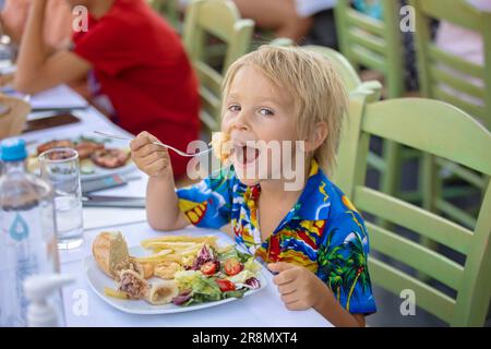 Süßes Kind, das im Sommer im Restaurant im Freien sitzt und Meeresfrüchte, Garnelen, Calamari, Tintenfisch und pommes frites isst Stockfoto