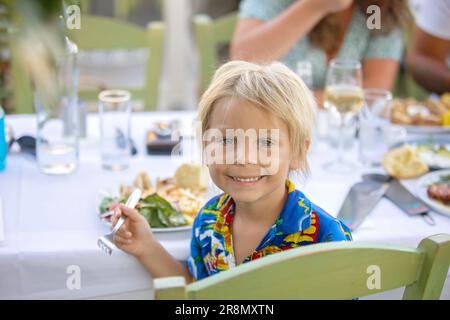 Süßes Kind, das im Sommer im Restaurant im Freien sitzt und Meeresfrüchte, Garnelen, Calamari, Tintenfisch und pommes frites isst Stockfoto