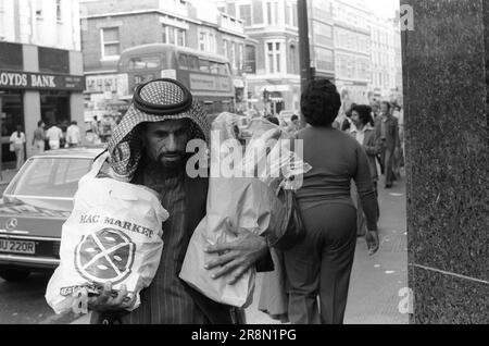 Arme Araber in London, Einkaufen für Lebensmittel. In den späten 1970er Jahren sorgten die Regierungen des Nahen Ostens für die Gesundheitsversorgung ihrer Staatsangehörigen in London, viele blieben in billigen Schlafzimmern in der Gegend von Earls Court. Ein Araber führt zwei Einkaufstüten mit Lebensmitteln aus. Earls Court, London, England, ca. 1977 70s GB HOMER SYKES Stockfoto