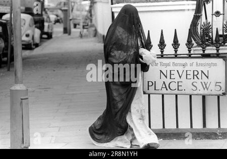 Arme Araber in London 1970er. Menschen aus dem Nahen Osten kamen nach Großbritannien für subventionierte Gesundheitsversorgung in Harley Street Kliniken. Sie haben hauptsächlich in billigen Hotels in Earls Court übernachtet. Eine Frau, die eine Burka trägt, die den ganzen Körper vom Kopf bis zum Boden bedeckt. Earls Court, London, England, ca. 1977 1970er GB HOMER SYKES Stockfoto