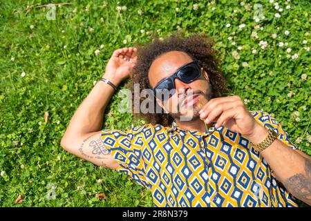 Afro-Haarmann mit Sonnenbrille im Sommer, der einen Urlaub oder Urlaubstag auf dem Gras genießt Stockfoto