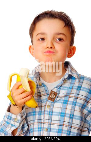 Der Junge isst Banane, den ganzen Mund, dicke Wangen Stockfoto