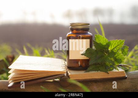 Naturheilkunde, Pillen in einem Glasbehälter. Öffnen Sie den alten Notizblock und den Medikamentenbehälter, frische Kräuter aus der Brennnessel Stockfoto