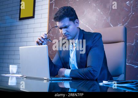 Ein müder indischer Geschäftsmann, der im Büro an einem Laptop arbeitet. Belastung durch Bildschirm, Workload-Konzept. Stockfoto