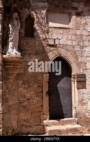 Die Fassade einer mittelalterlichen Kapelle mit einer Bogentür und einer Statue der Jungfrau Maria am Eingang, die sich auf der Straße der Ritter in Rhodos befindet. Stockfoto