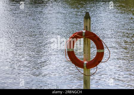 Rettungsboje hängt an einem Holzpfahl mit Wasser im Hintergrund. Stockfoto