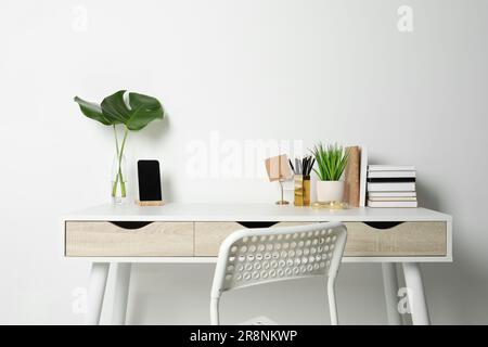 Komfortabler Arbeitsplatz mit weißem Schreibtisch an der Wand Stockfoto