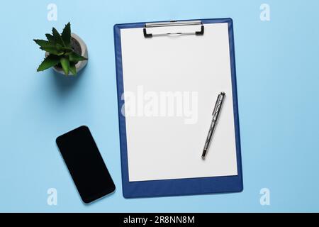 Kugelschreiber, Klemmbrett mit Papierbogen und Smartphone auf hellblauem Hintergrund, flach liegend Stockfoto