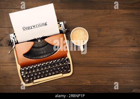 Word Copywriting auf Papier. Schreibmaschine und Tasse Kaffee auf Holztisch, flach liegend. Platz für Text Stockfoto