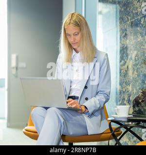 Schöne Geschäftsfrau, die am Tisch sitzt und an einem Laptop arbeitet. Stilvolle Frau in einer modernen Büroumgebung Stockfoto