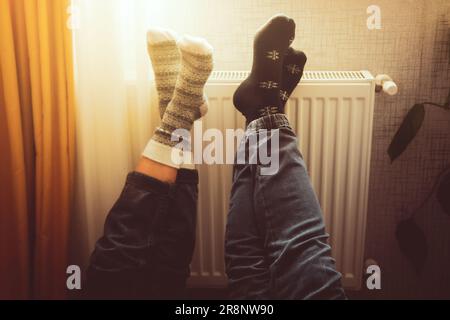 Halten Sie die Beine hoch, heizen Sie die Füße in kalten Wohnungen drinnen auf der Heizung im Winter mit kuscheligen Wintersocken an. Valentinsgeschenk mit warmen Füßen am Heizkörper Stockfoto