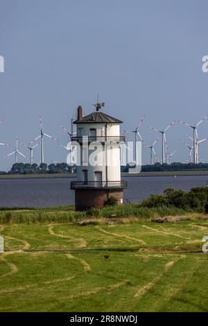 Ein malerischer Blick auf einen Leuchtturm an einer grünen Küste mit mehreren Windturbinen im Hintergrund Stockfoto