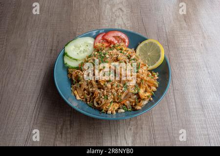 Asiatische Dishe kulinarisches Stillleben. Pad Thai Nudeln mit Huhn, Samen, Tomaten, Gurken und Zitrone Stockfoto