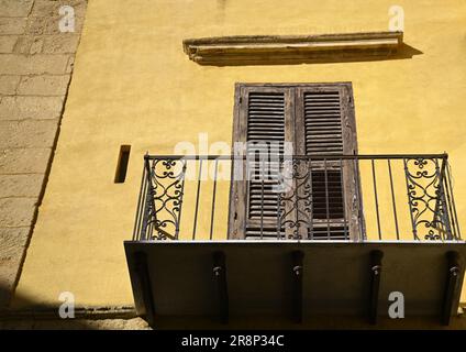 Alte neoklassizistische Fassade mit ockerfarbenen Stuckwänden, Fensterläden aus Holz und einem Balkon mit schmiedeeisernem Geländer in Agrigento Sizilien, Italien. Stockfoto