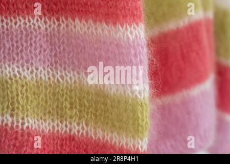 Nahaufnahme eines handgestrickten Pullover aus pinkfarbenem, weißem und grünem Bonbon mit gestreiftem Mohair-Garn und Stickerei mit Strümpfen und Rippen. Stockfoto