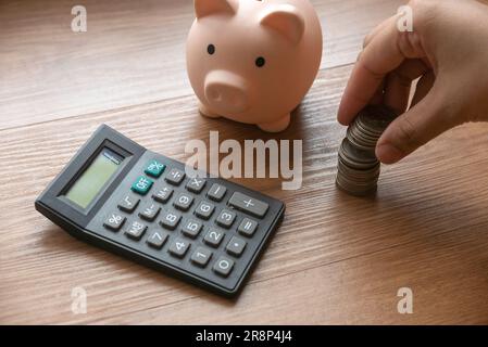 Geschäfts- und Finanzkonzept mit einer Hand, die einen Münzstapel hält, Sparschwein und Taschenrechner. Stockfoto