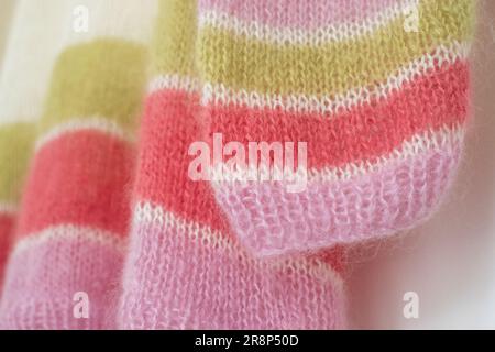 Nahaufnahme eines handgestrickten Pullover aus pinkfarbenem, weißem und grünem Bonbon mit gestreiftem Mohair-Garn und Stickerei mit Strümpfen und Rippen. Stockfoto
