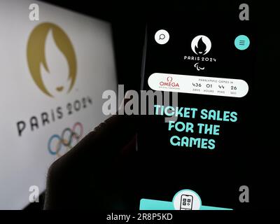 Person, die ein Mobiltelefon mit einer Webseite der Olympischen Sommerspiele 2024 in Paris auf dem Bildschirm vor dem Logo hält. Konzentrieren Sie sich auf die Mitte des Telefondisplays. Stockfoto