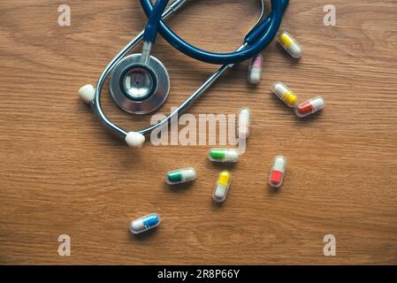 Draufsicht des Stethoskops und verschütteter Pillen auf Holzhintergrund. Stockfoto