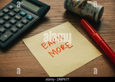 Selektiver Fokus auf Taschenrechner, Geldschreiber und Papier, geschrieben mit Earn More. Stockfoto