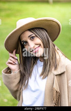 Eine junge Frau, die auf einem üppigen grünen Feld steht und einen Hut mit breiter Krempe trägt, mit einem Baum im Hintergrund Stockfoto