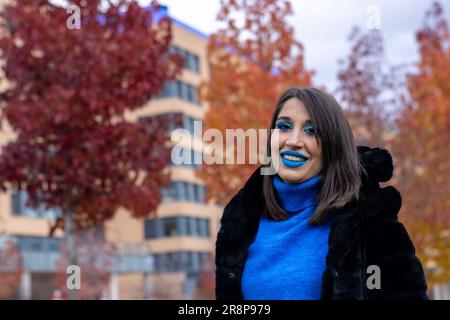 Eine junge weiße Frau mit blauem Lippenstift und schwarzem Teddybärmantel steht mit einer selbstbewussten und entspannten Pose Stockfoto