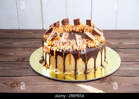 Herrlicher Snickers-Kuchen mit Erdnussbutter-Sahne, geschmolzener Schokolade, Schokoriegeln und gesalzenem Karamell Stockfoto