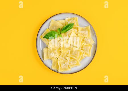 Leckeres, appetitliches Ravioli mit Käse und Basilikum auf einem Teller, hellgelber Hintergrund Stockfoto